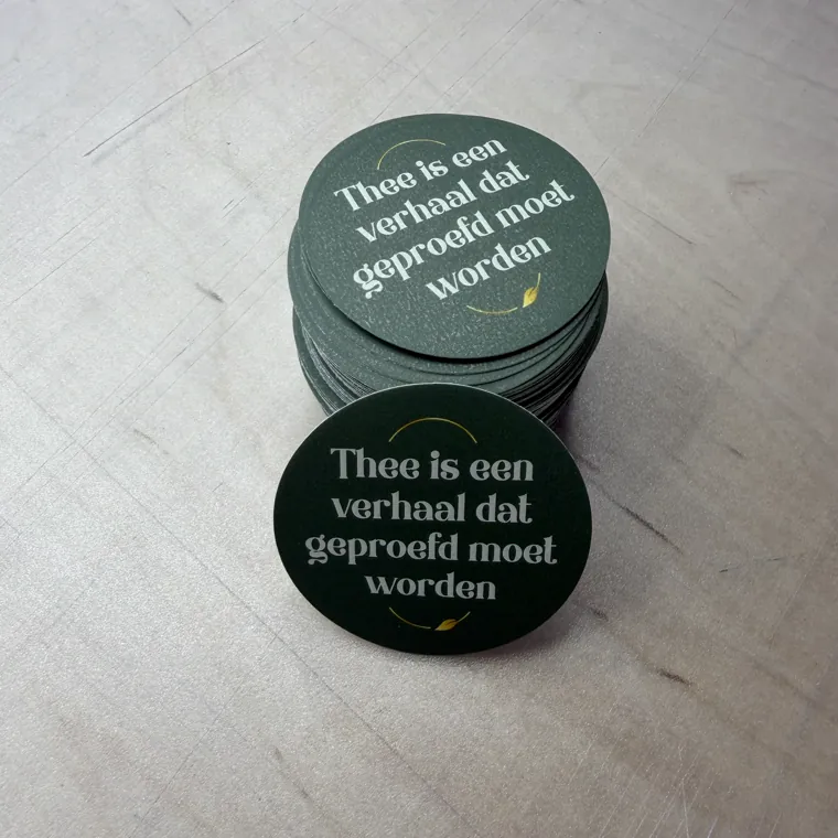 Stapel losse ronde stickers met een donkergroen tekstontwerp op een werktafel